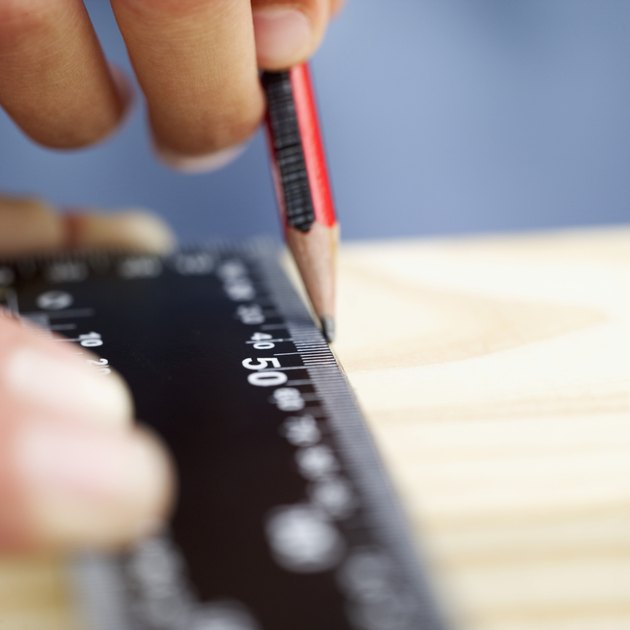 close-up of a person's hands marking a wooden plank with a ruler and a pencil
