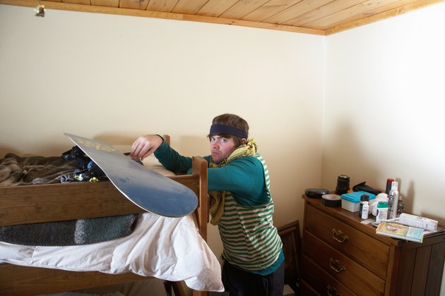 Young man leaning on bunk bed with snowboard, portrait
