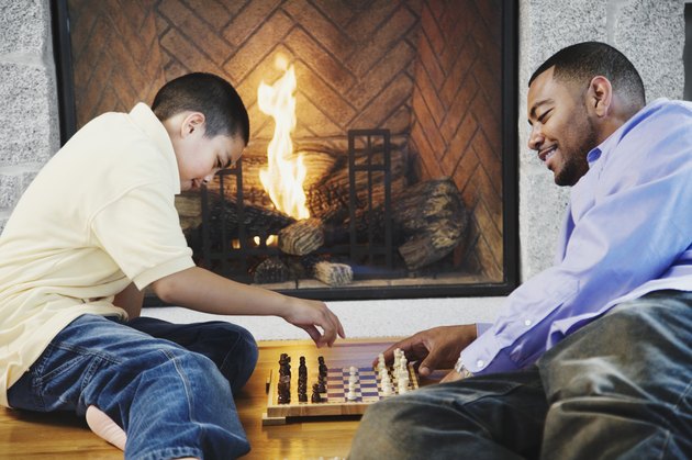 Father and son playing chess by fireplace