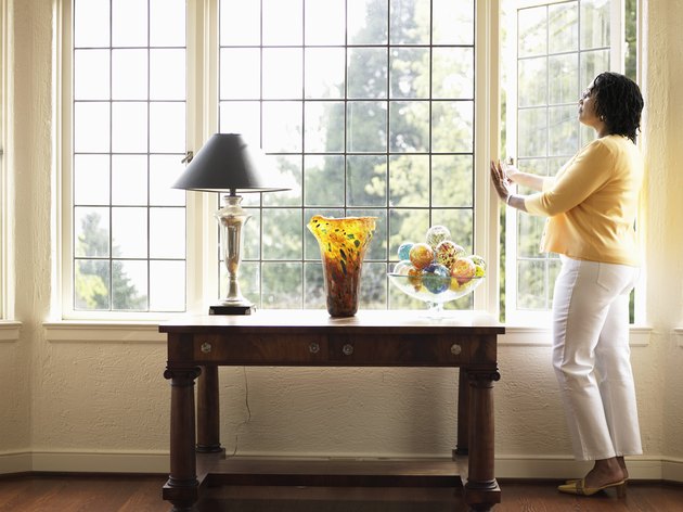 Mature woman looking out open window in living room, side view