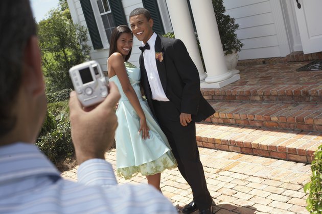 Man photographing young couple wearing evening dress, outdoors,smiling