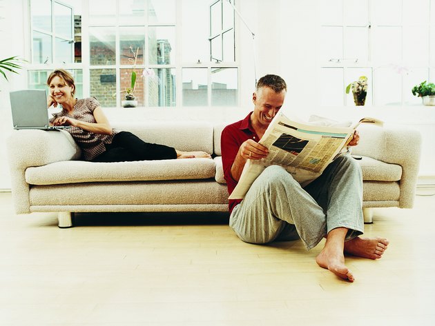 Business Couple Sitting in a Living Room Apartment Reading the Newsapaper and Using a Laptop