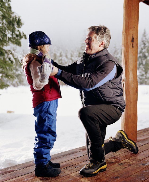 Father tying daughter's (6-8) scarf on porch, winter, side view