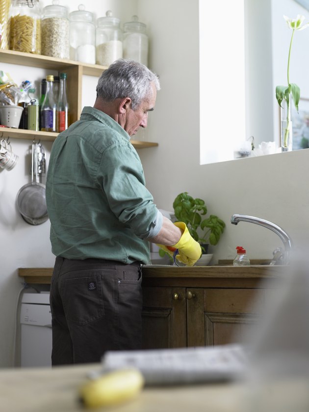 Senior man wearing rubber gloves washing up at sink (focus on man)