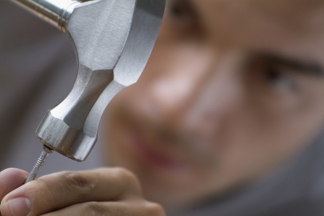 Man hammering nail, focus on hammer and nail, close-up