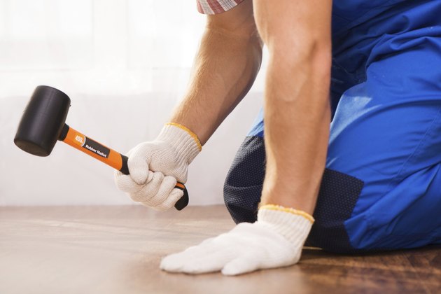 Close-up photo of repairman hammering fabricated wood block flooring