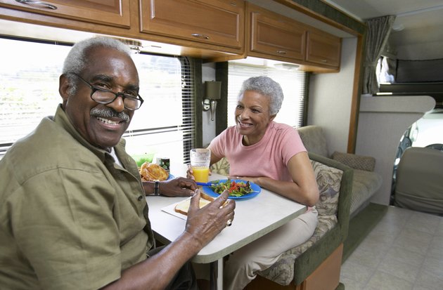 Senior Couple Sit at a Table in a Motor Home, Having Lunch