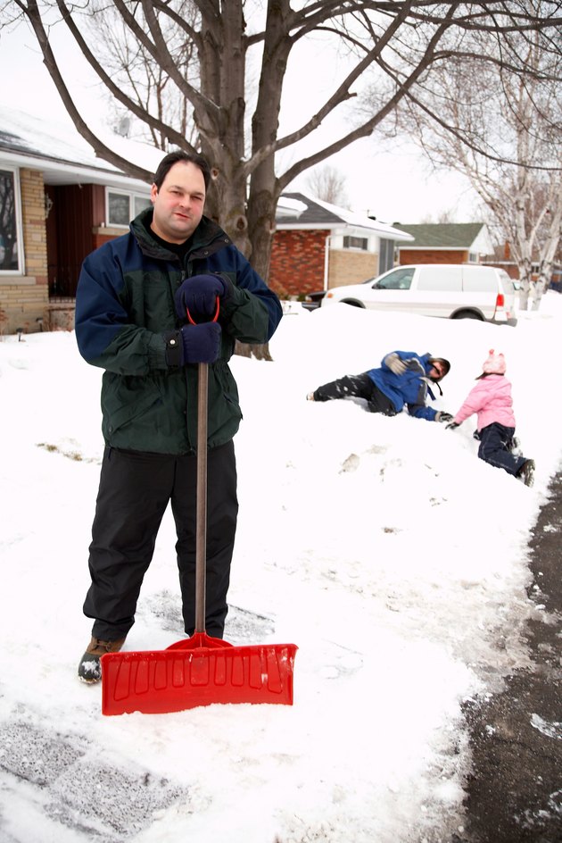 Father posing with snow shovel while children play