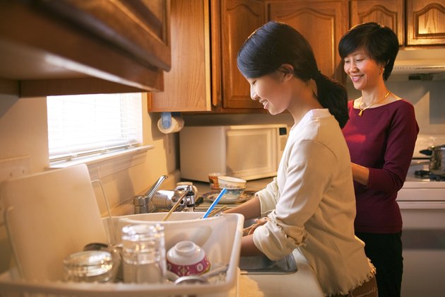 A mother and daughter stand in the kitchen doing the dishes