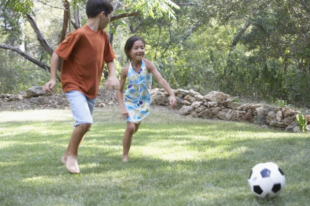 Front profile of a boy and a girl playing football in a garden