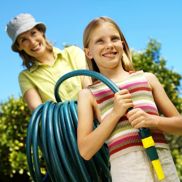 portrait of a mother and daughter holding a garden hose in the yard