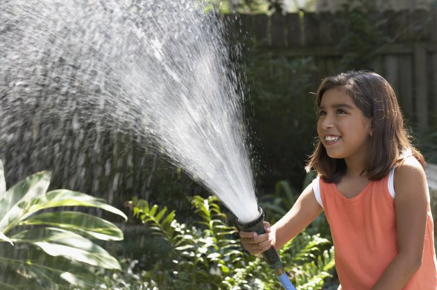 Side profile of a girl watering a garden with a hose