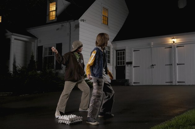 Two boys (12-13) standing in driveway, throwing eggs at house, night, rear view