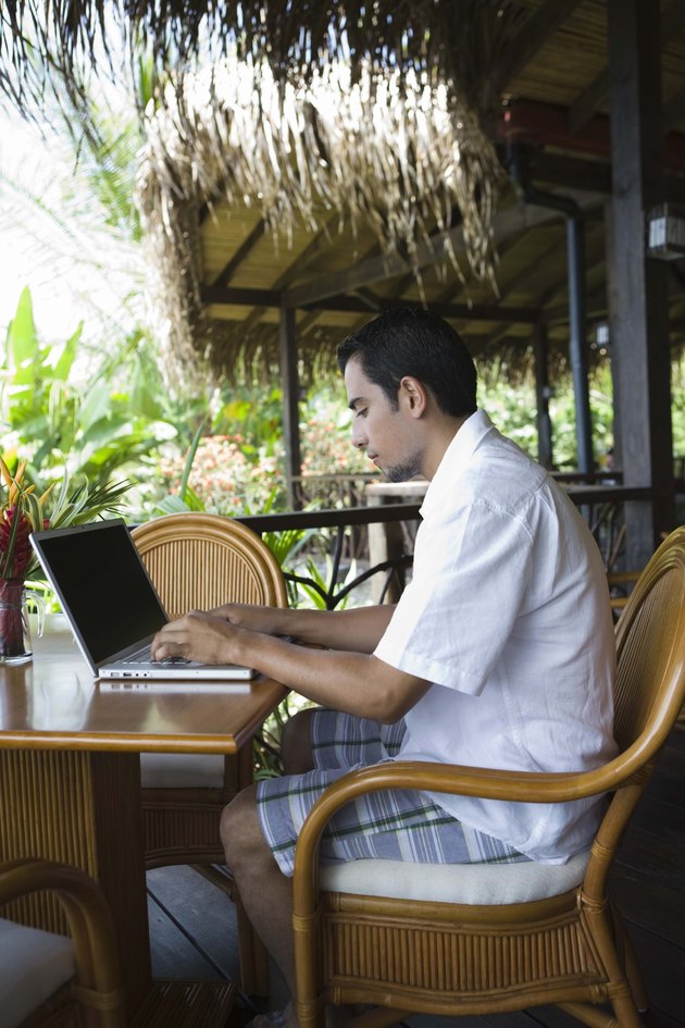 Man working on laptop computer in tropical cafe