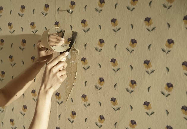 Close up of a hand scraping away wallpaper