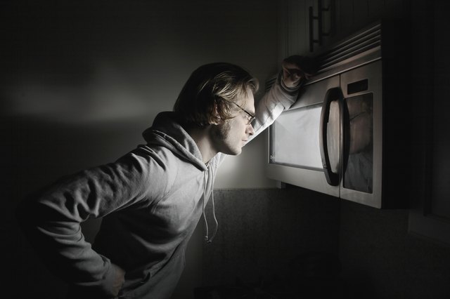 Young man looking in microwave window, side view