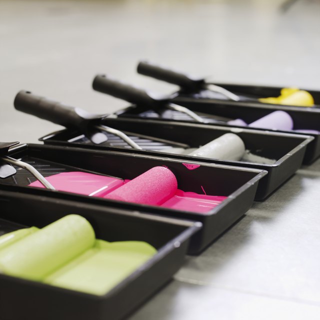 Close-up side view of trays of coloured paint and paint rollers