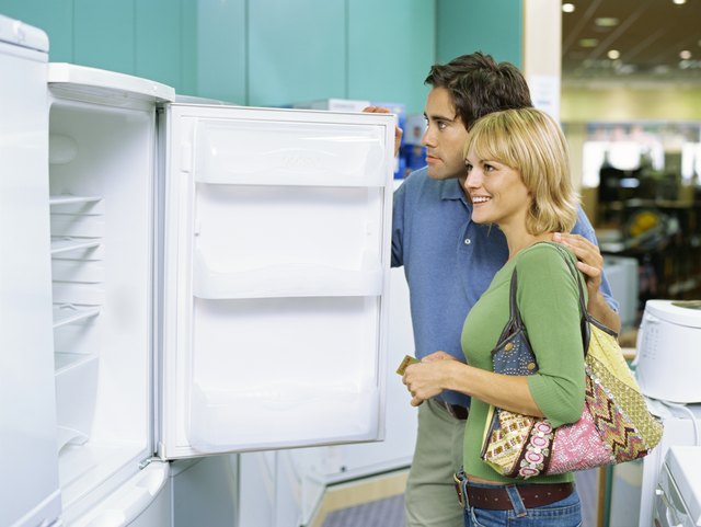 side profile of a young couple looking at an open refrigerator in an electronics store
