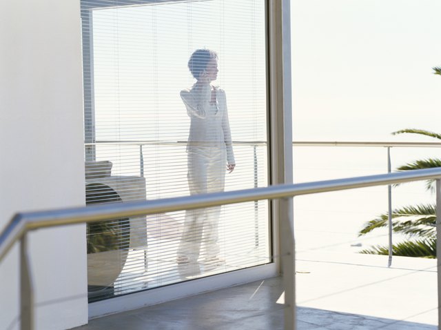mid adult woman standing behind blinds and talking on a mobile phone
