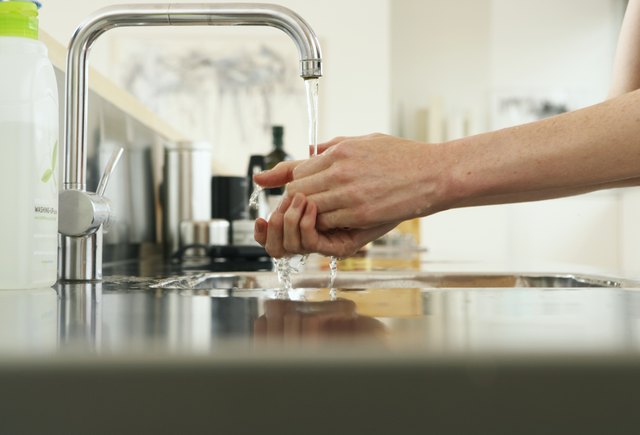 Woman washing hands at kitchen sink, view along counter, close-up