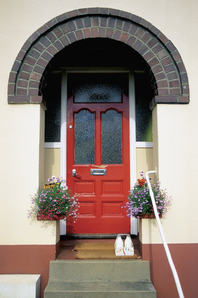 Bottles of milk and hanging plants outside house with red door in Totnes, England