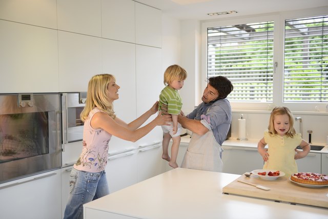 Mature man using cell phone and passing son to woman in kitchen