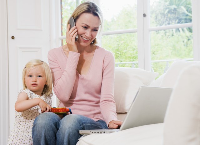 Child playing by mother talking on phone and working on computer