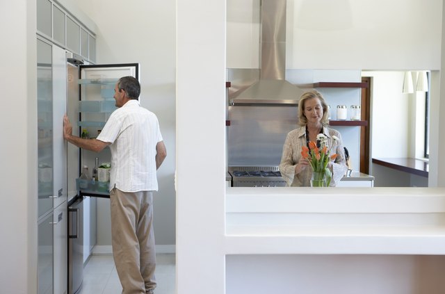 Couple in kitchen, man looking in fridge, woman arranging flowers