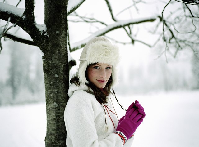 Young woman standing in snow, leaning against tree, portrait