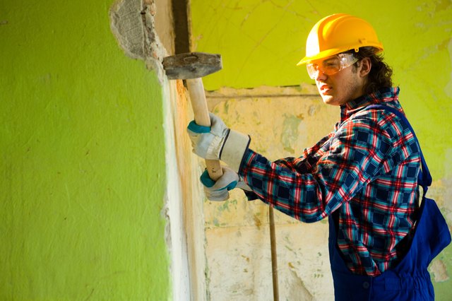 Construction worker demolishing wall with sledgehammer