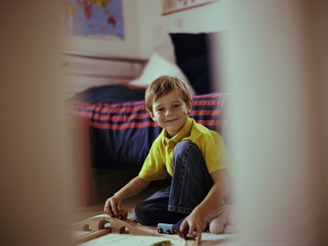 Boy (5-7) playing train sets in bedroom, smiling, portrait