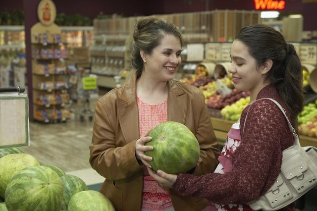 Mid adult woman and her daughter holding a watermelon in a supermarket