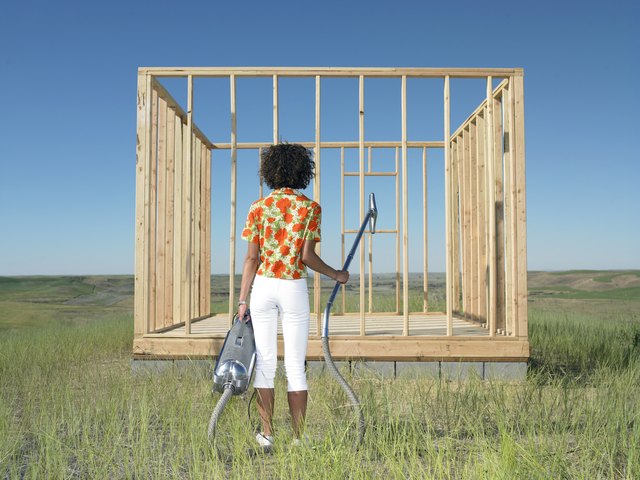 woman standing with vaccuum in front of frame hous