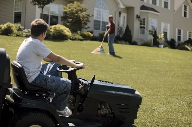 Boy on tractor mower with father raking lawn