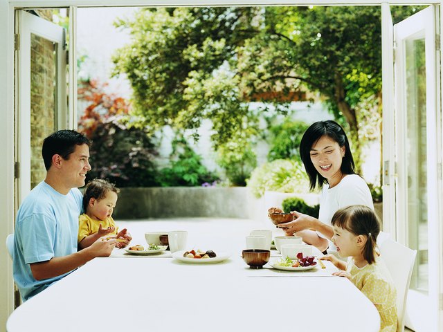 Family of Four Dining at a Table With French Windows Open Onto a Courtyard