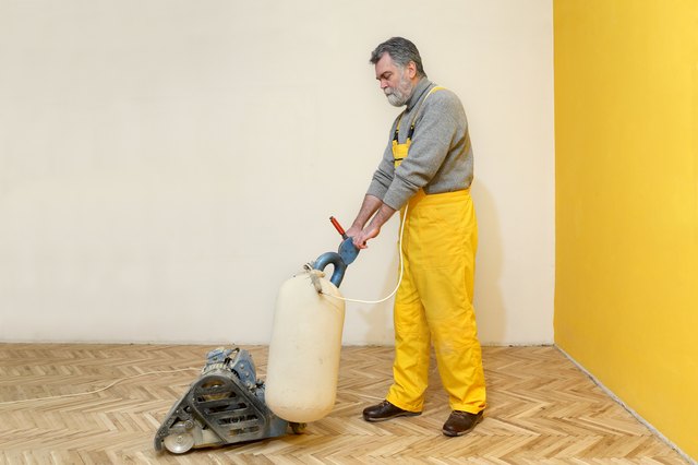 Worker polishing old parquet floor with grinding machine