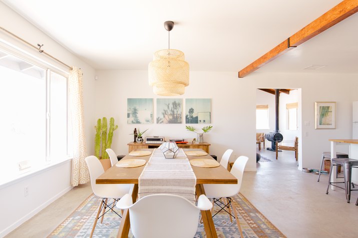 a solid wooden dining table under a large rattan pendant lamp in a spacious open-plan house