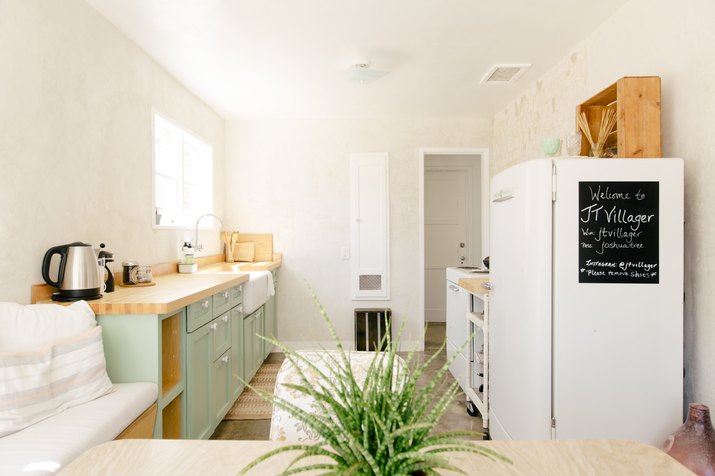 a narrow kitchen has a row of green cabinets on one wall, and the refrigerator and stove along another