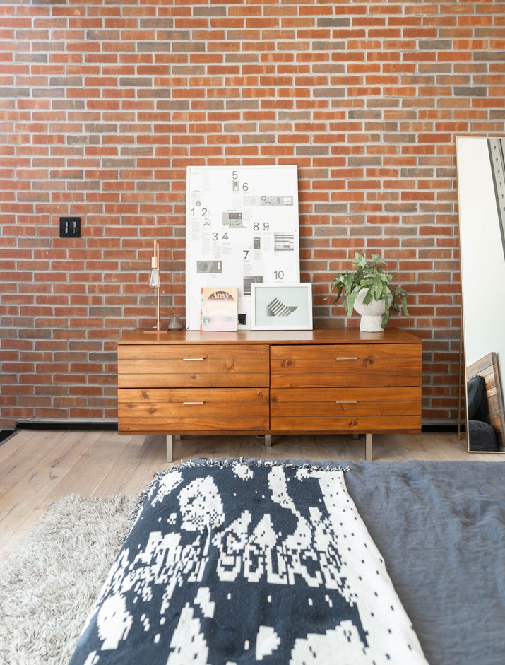 Contemporary bedroom with wood cabinets, lamp, plant, white diagram board, brick wall, full-length mirror, and black-and-white bed