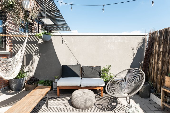 Outdoor contemporary patio with canopy, wood benches with pillows, silver metal chairs, and dried bamboo fence