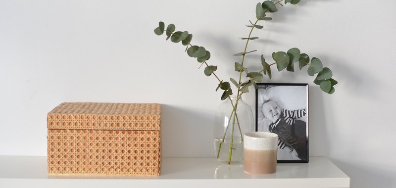 Cane box on white shelf with vase with eucalyptus