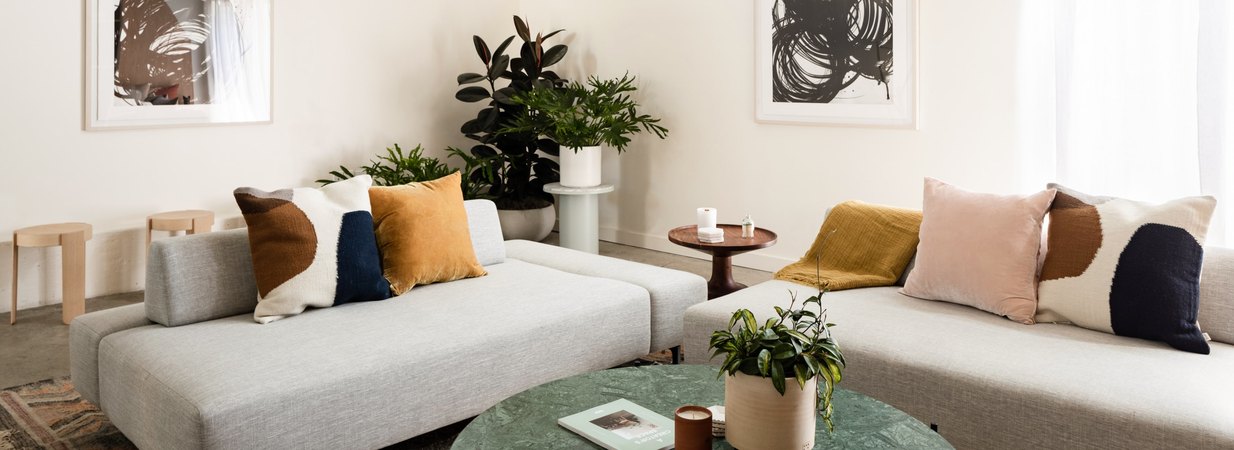 Living room couches filled with pillows and surrounded by plants